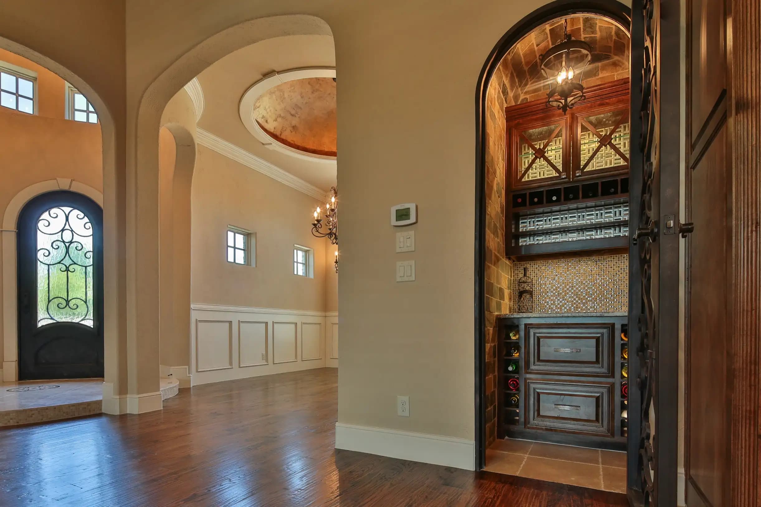 Entryway with arched doorways, wood floors, decorative ceiling detail and a built-in wine nook with iron door and dark wood cabinetry
