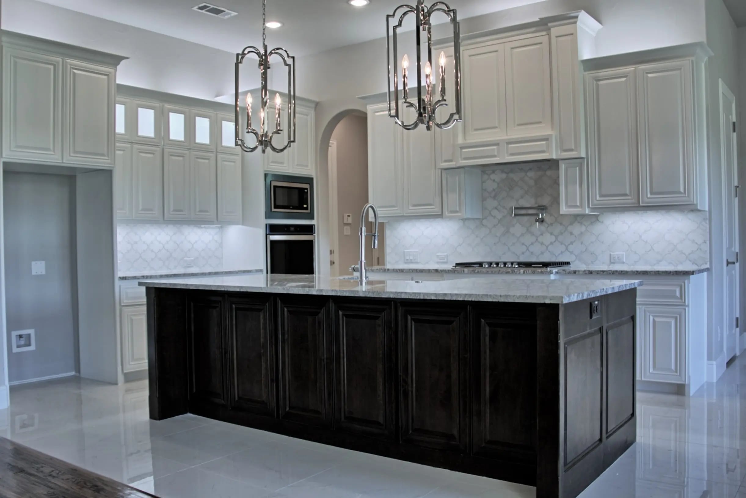 Kitchen with white upper cabinets, dark wood island, stainless steel appliances, marble countertops and pendant lights