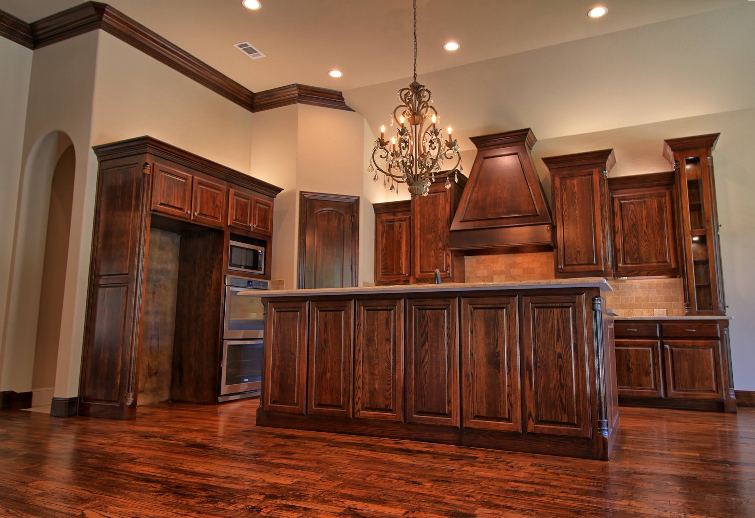 Kitchen with stained oak cabinetry and crown molding, paneled island, tapered wood hood, double wall ovens, crystal chandelier and hand-scraped hardwood floors