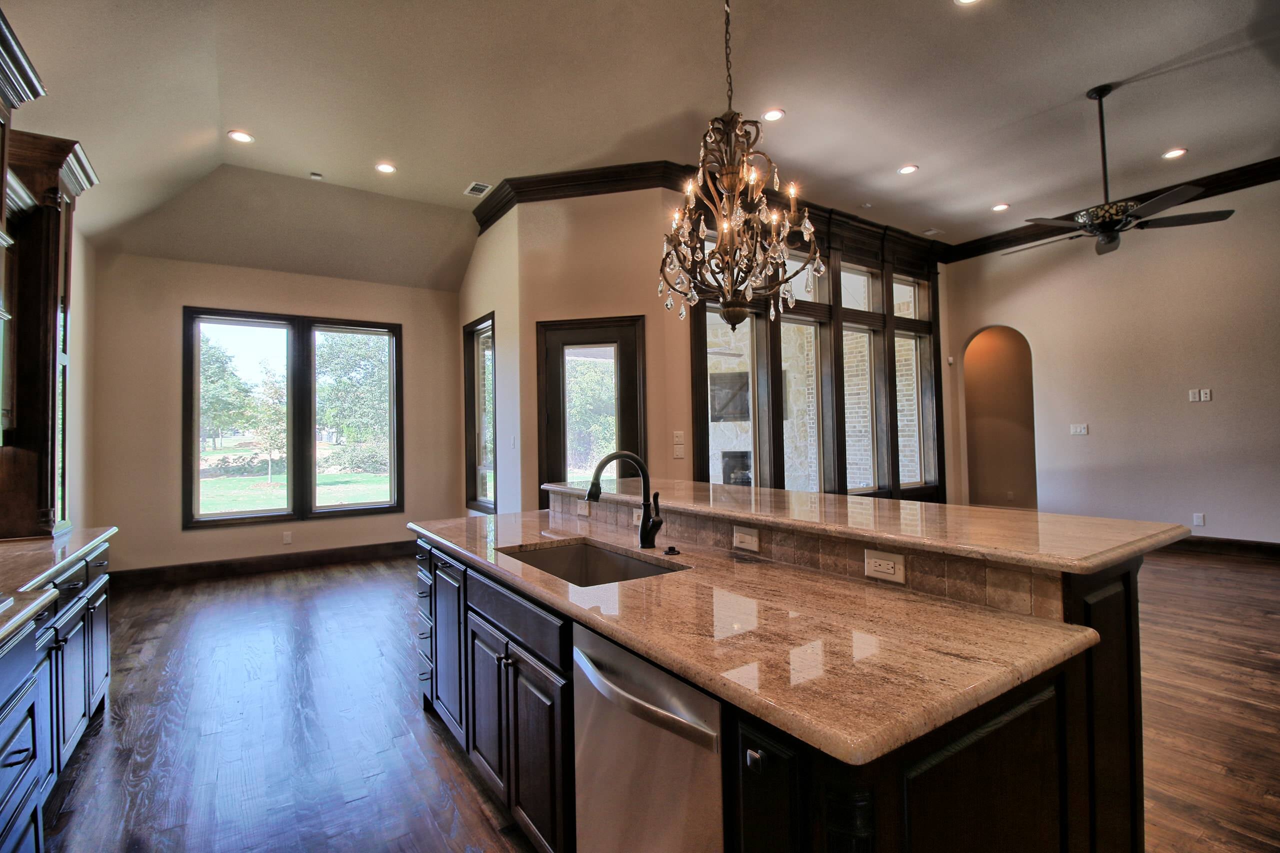 Granite kitchen island with raised bar, undermount sink and crystal chandelier, open to a vaulted nook and living area with tall windows