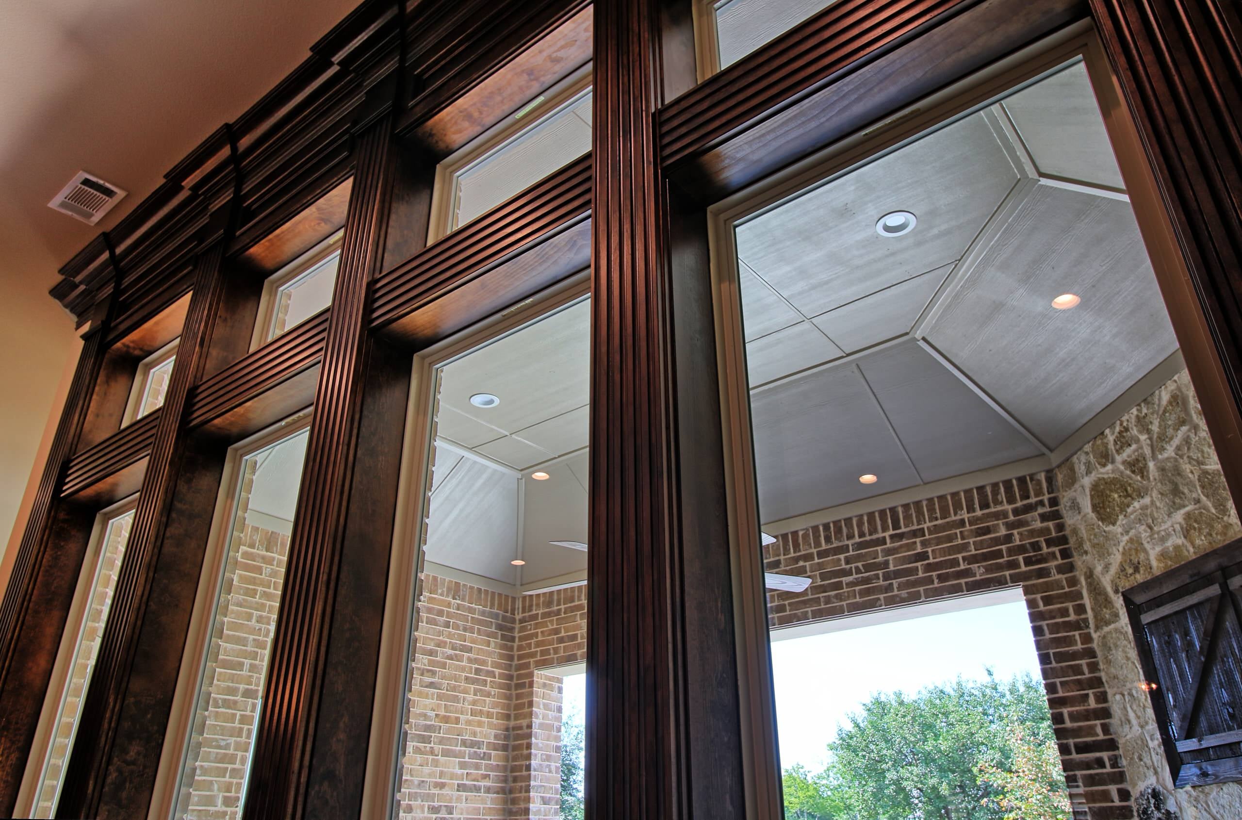 Tall windows with transoms in fluted stained wood casings, looking out to a covered brick patio with stone wall and recessed lights