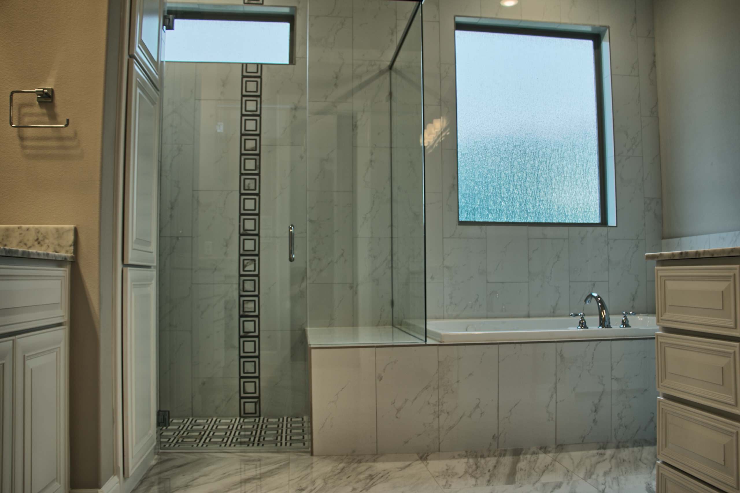 Frameless glass shower with marble-look tile, black-and-white mosaic accent and bench beside a tiled drop-in tub under a textured glass window