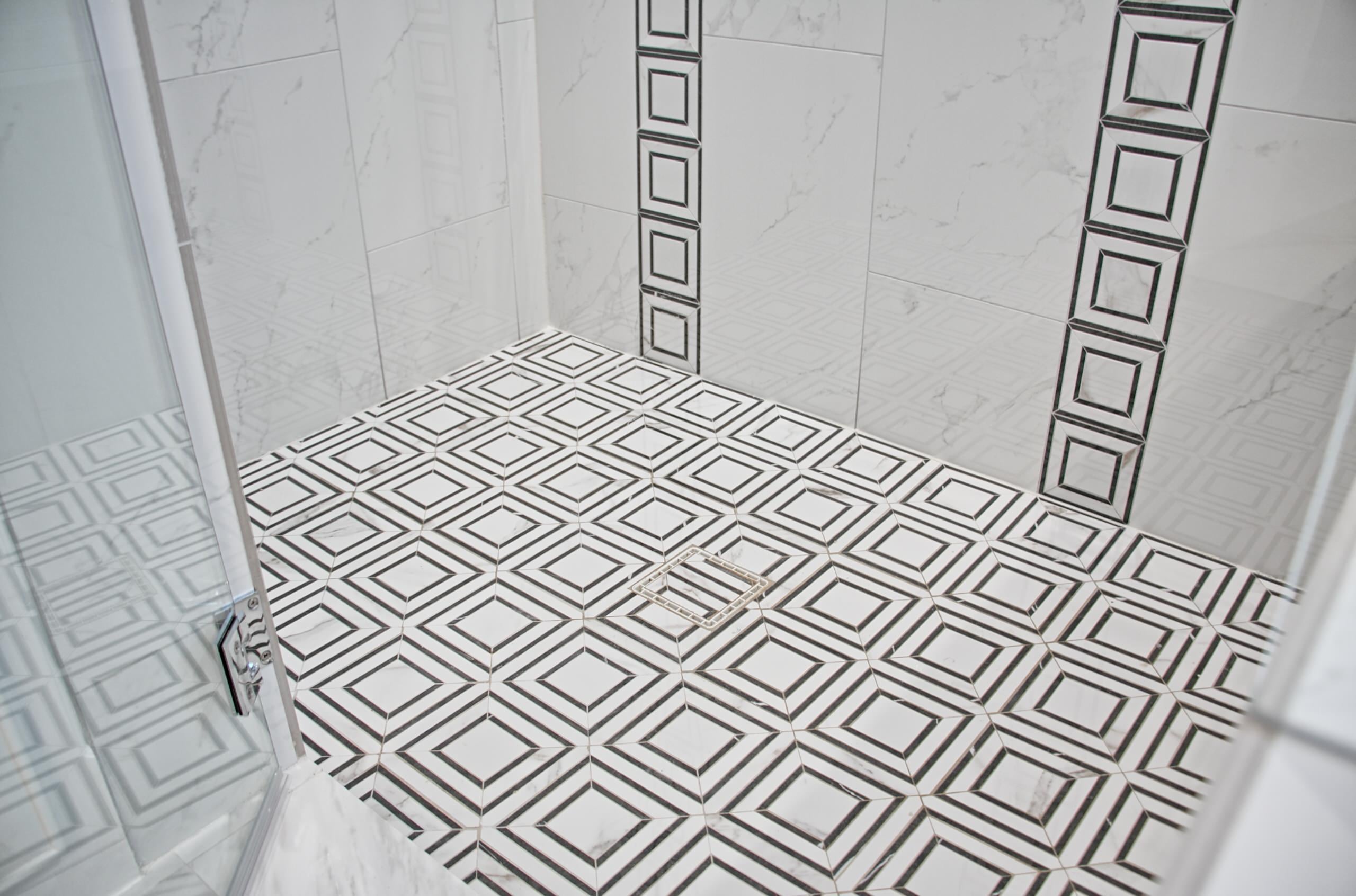 Shower floor in black-and-white geometric mosaic tile with square drain, framed by marble-look wall tile with black-and-white mosaic accent strips